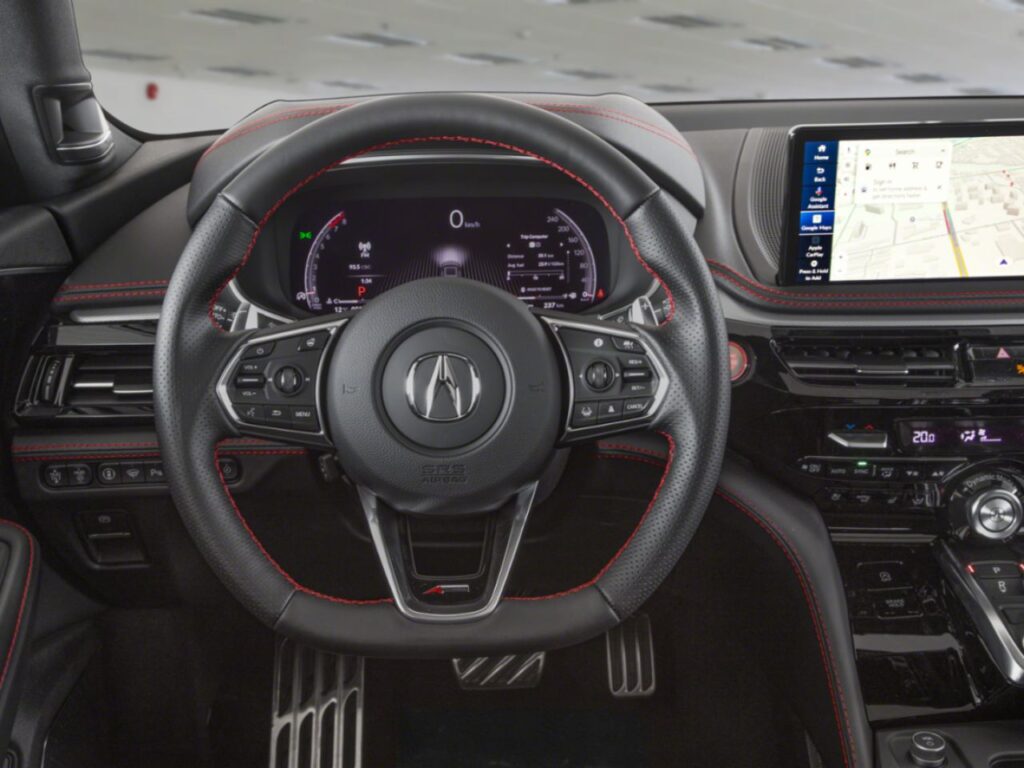 Intérieur d’un Acura MDX avec volant sport en cuir à surpiqûres rouges, tableau de bord numérique, écran multimédia avec navigation intégrée et console centrale haut de gamme orientée vers le conducteur.